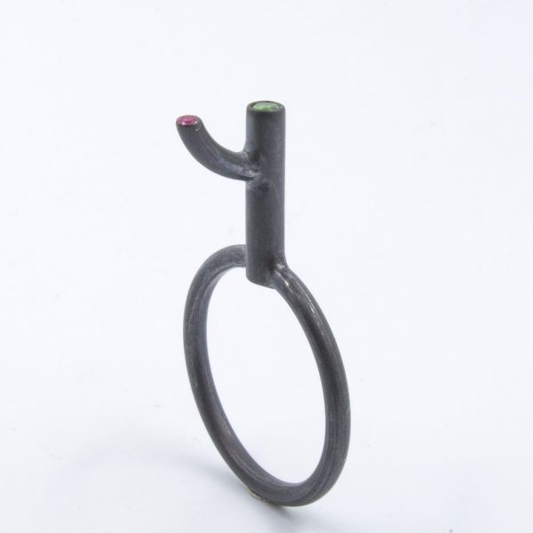 Anillo-colgante de plata ennegrecida con tsavorita (granate verde) y rubí. Se vende con cordón "cola de topo" trojo o negro, de 50cm. El diseño de esta serie de anillos-escultura hace referencia a la expresión española "irse por las ramas", que significa cambiar de tema deviando el discurso. Talla 14 Altura sobre el dedo 14mm Objeto diseñado y fabricado en Madrid por personas que disfrutan su trabajo, y celebran la riqueza de su lengua materna.